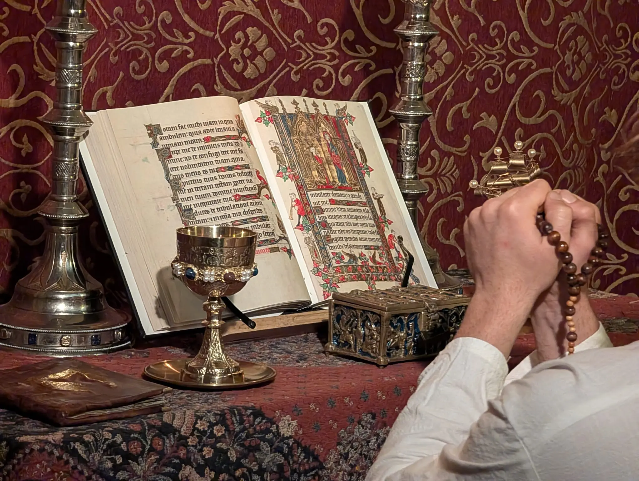 Close-up of hands together in prayer in front of a replica manuscript and ornate golden display pieces