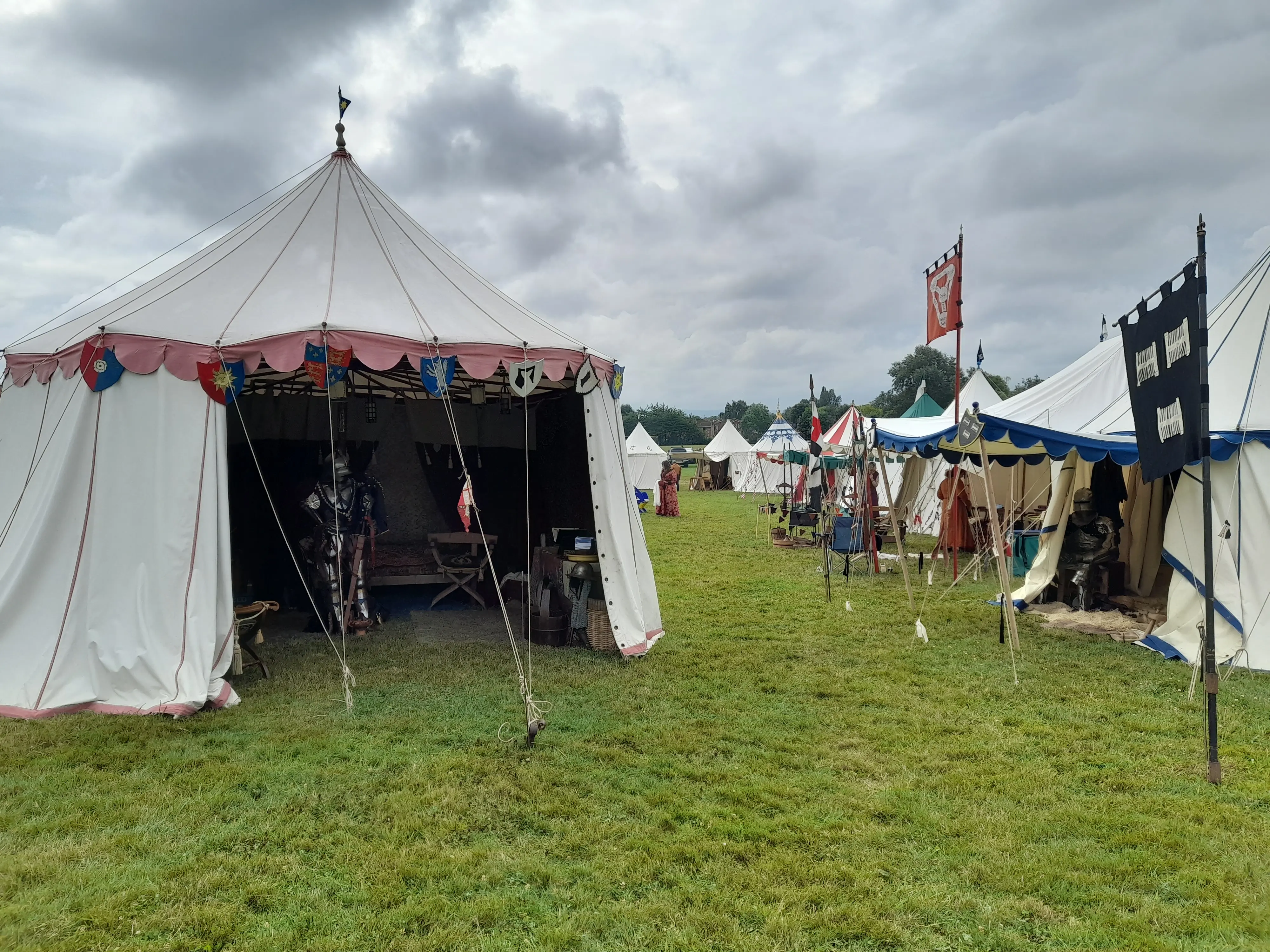 Several medieval tents at a re-enactment camp, one open with a suit of armour inside