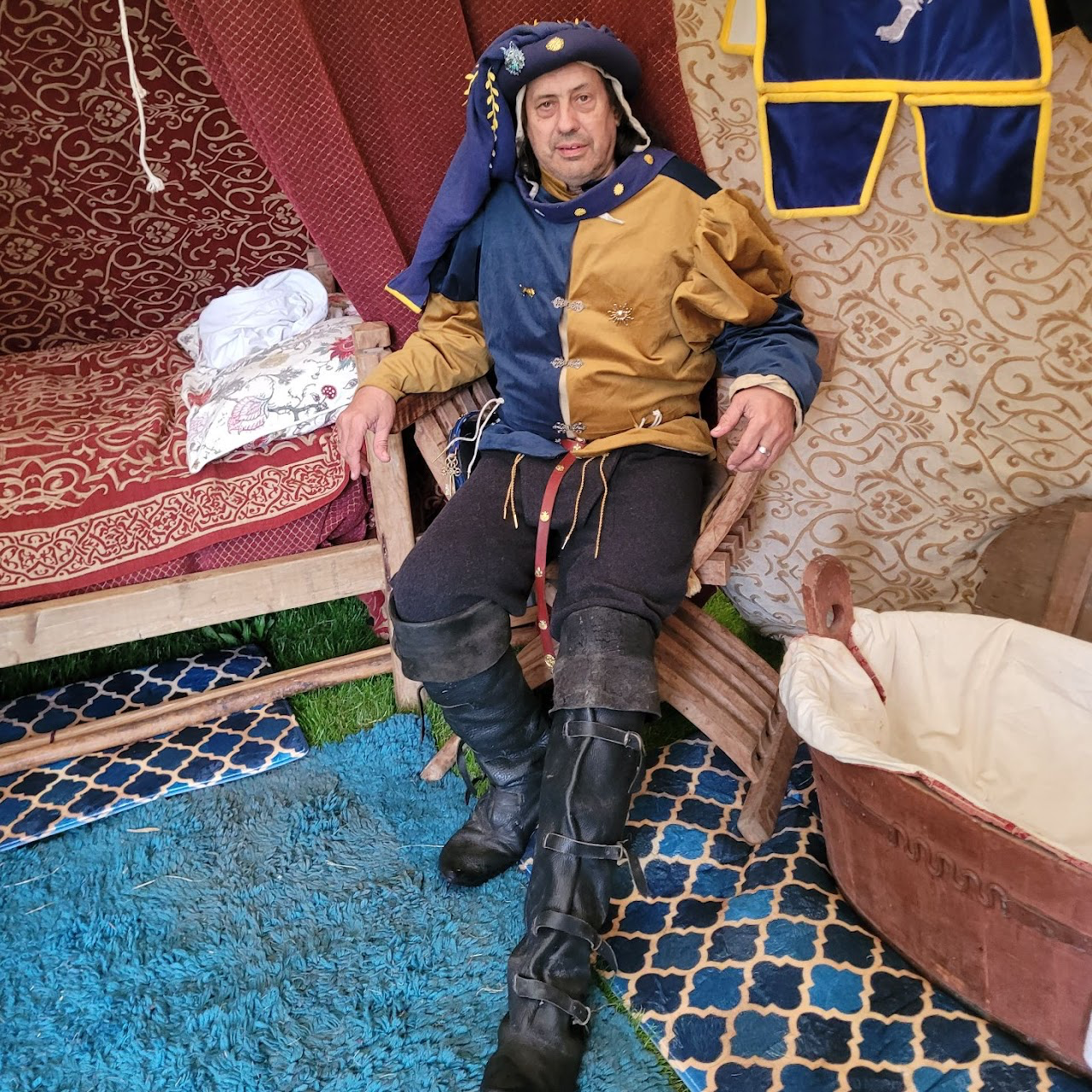 Mike Bass as Sir John Dunne sitting in a chair inside a medieval tent