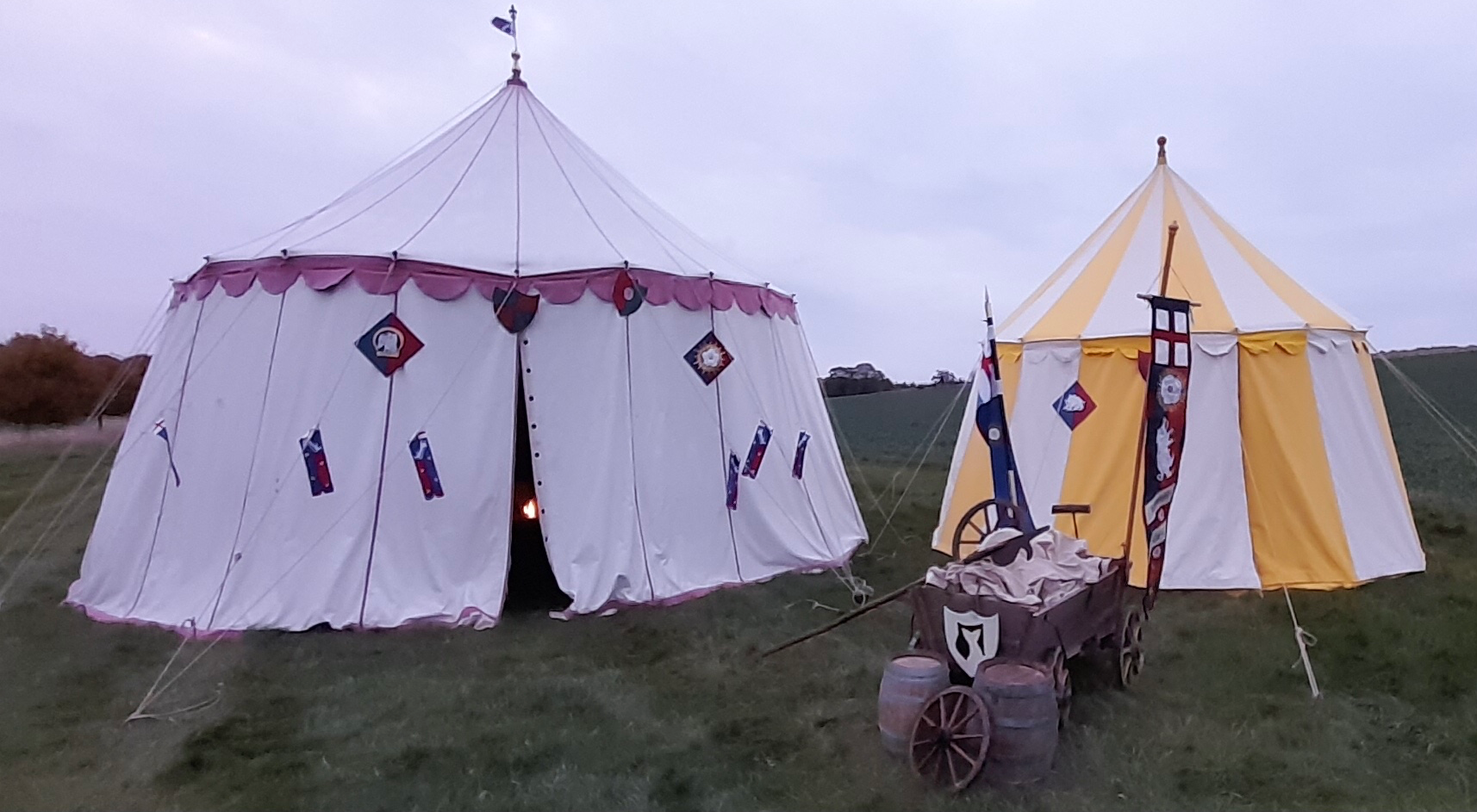 A wooden cart and barrels with two medieval tent behind