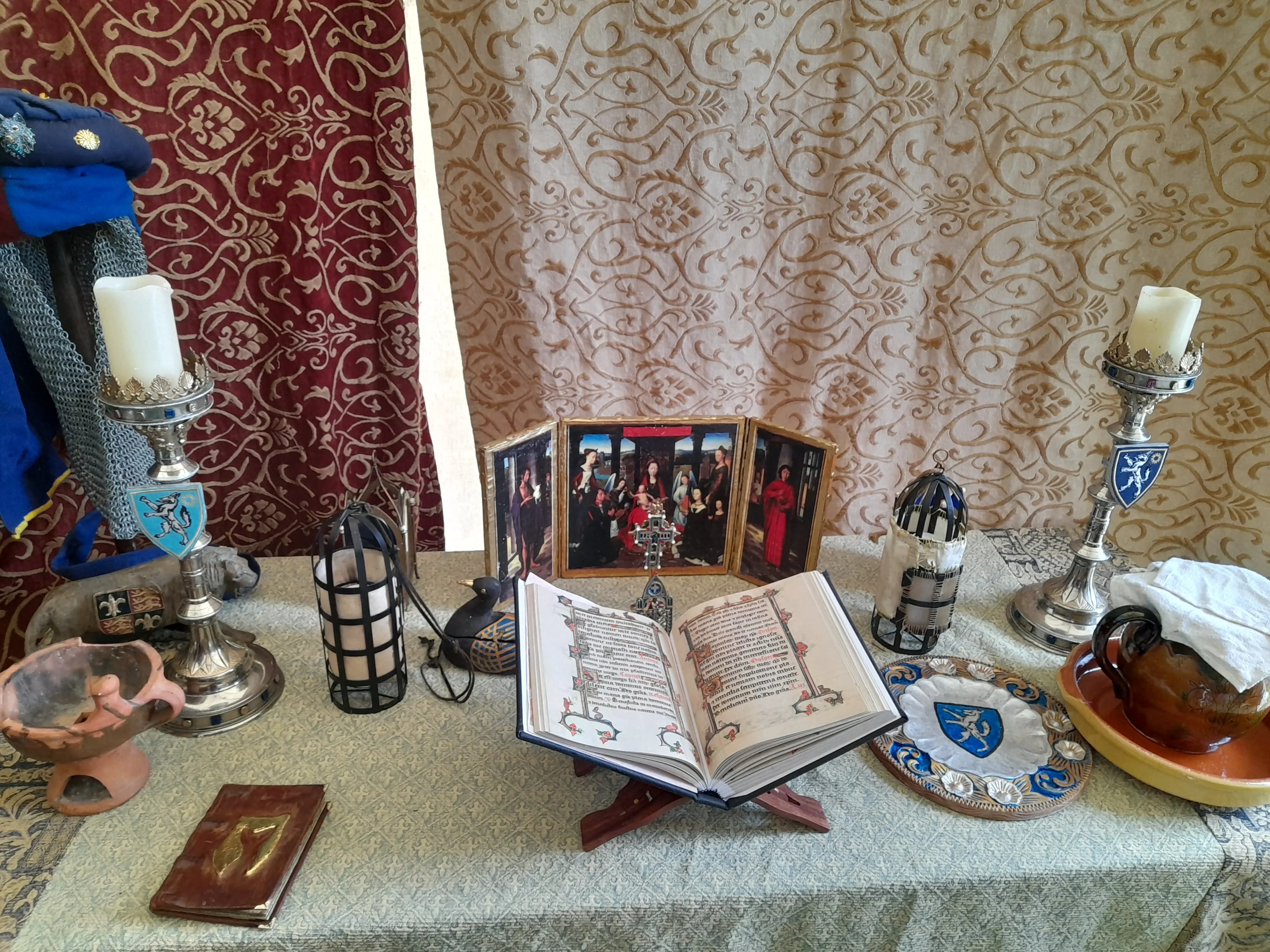 A table showing religious items including an old book, large metal candle holders and at the back the Donne Triptych replica